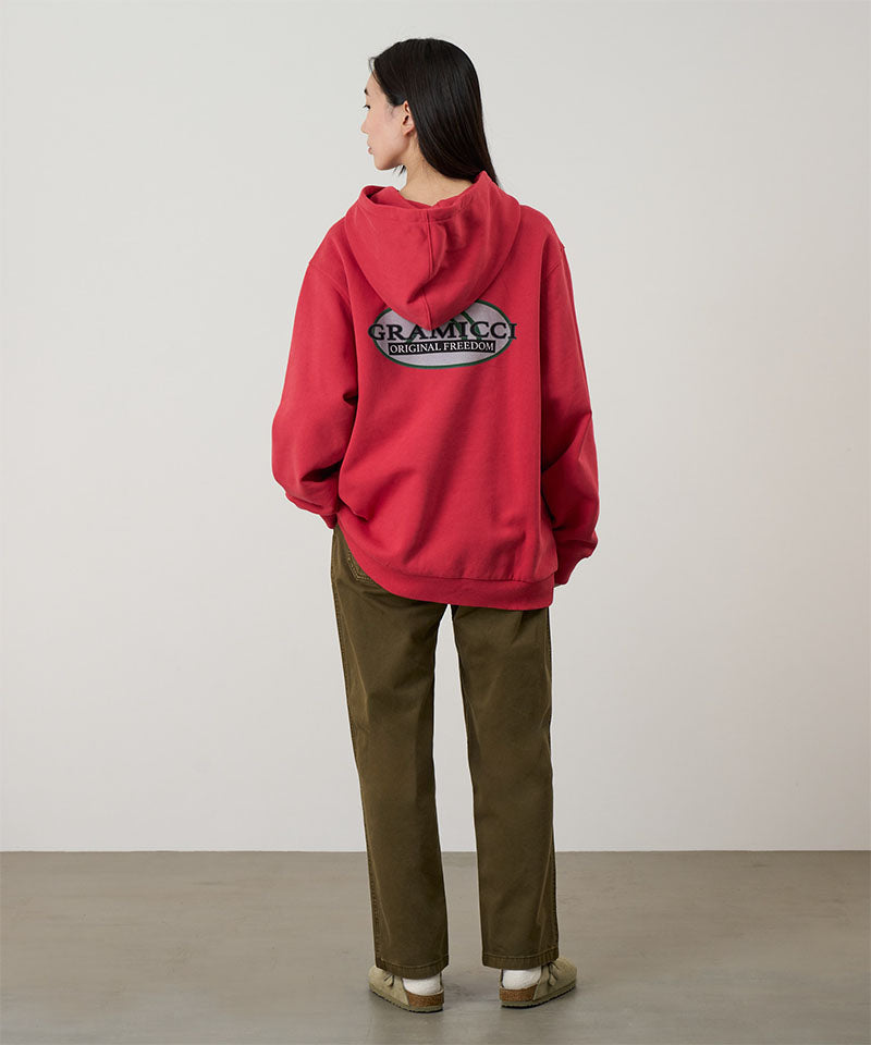 Back view of a model wearing bark pigment colored Gramicci Women's Brooks Pants and a red hoodie on a light-tone background.