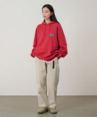 Model wearing sand pigment colored Gramicci Women's Brooks Pants and a red hoodie on a light-tone background.