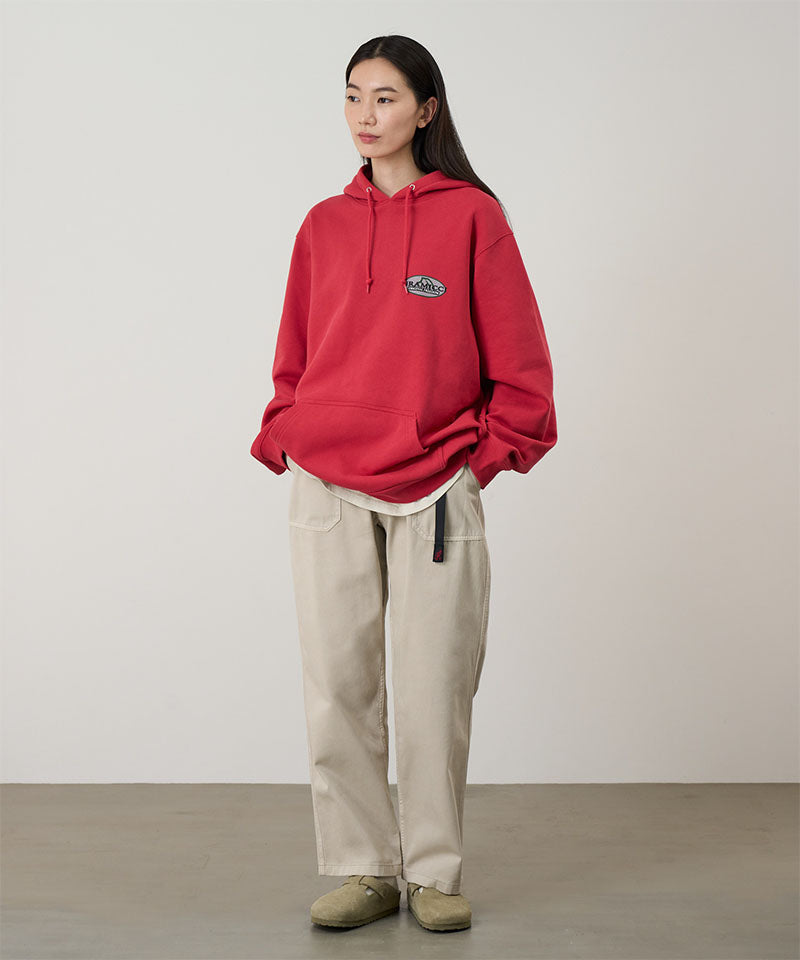 Model wearing sand pigment colored Gramicci Women's Brooks Pants and a red hoodie on a light-tone background.