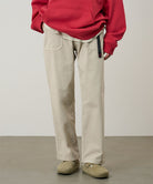 Model wearing sand pigment colored Gramicci Women's Brooks Pants and a red hoodie on a light-tone background.