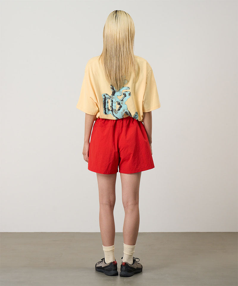 Back view of a model wearing burnt orange Gramicci Women's Nylon Active Short and a yellow shirt on a light-tone background.