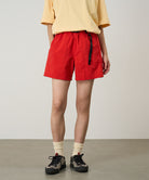 Model wearing burnt orange Gramicci Women's Nylon Active Short and a yellow shirt on a light-tone background.