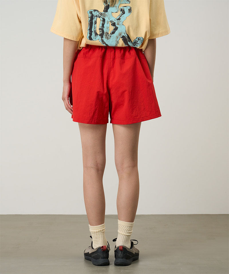 Back view of a model wearing burnt orange Gramicci Women's Nylon Active Short and a yellow shirt on a light-tone background.