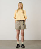 Model wearing milk tea Gramicci Women's Nylon Active Short and a yellow shirt on a light-tone background.