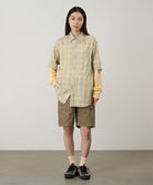 Model wearing beige Gramicci Women's Corduroy Utility Short and a green plaid shirt on a light-tone background.