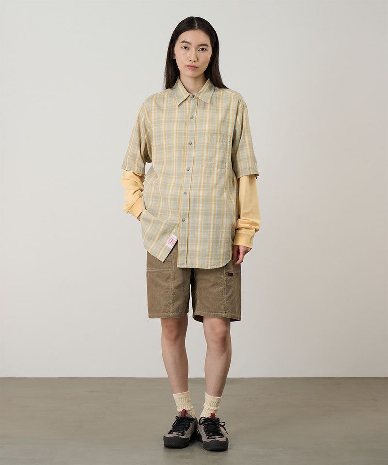 Model wearing beige Gramicci Women's Corduroy Utility Short and a green plaid shirt on a light-tone background.