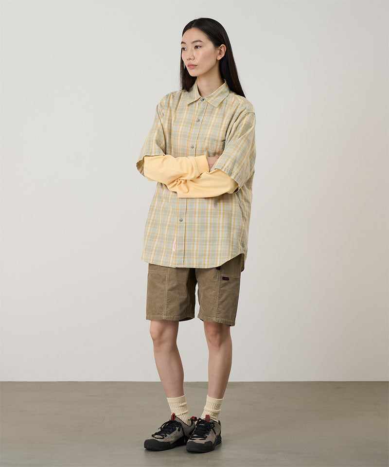Model wearing beige Gramicci Women's Corduroy Utility Short and a green plaid shirt on a light-tone background.