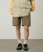 Model wearing beige Gramicci Women's Corduroy Utility Short and a green plaid shirt on a light-tone background.