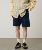 Model wearing beige Gramicci Women's Corduroy Utility Short and a green plaid shirt on a light-tone background.
