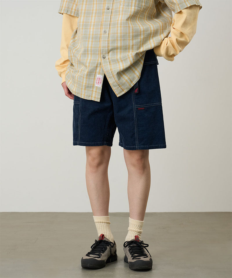 Model wearing beige Gramicci Women's Corduroy Utility Short and a green plaid shirt on a light-tone background.