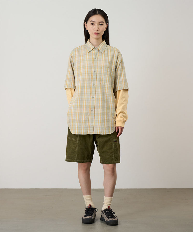 Model wearing olive Gramicci Women's Corduroy Utility Short and a green plaid shirt on a light-tone background.