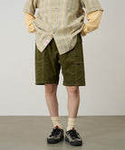 Model wearing olive Gramicci Women's Corduroy Utility Short and a green plaid shirt on a light-tone background.