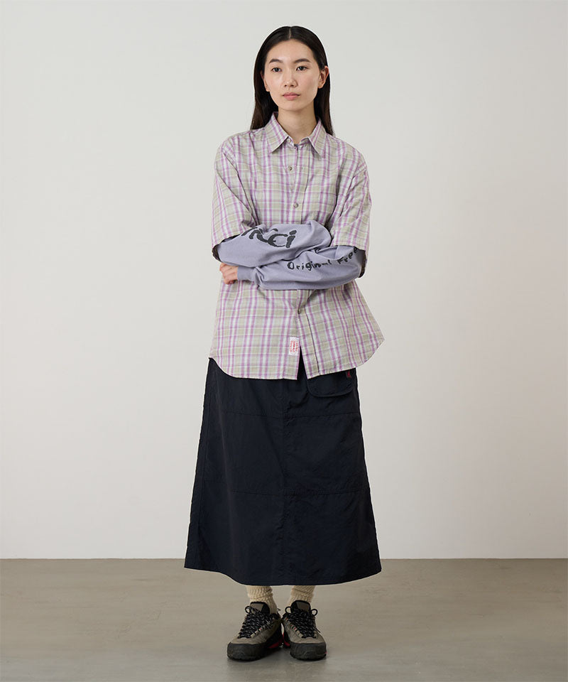 Model wearing a black Gramicci Nylon Utility Skirt and plaid shirt on a light-tone background.