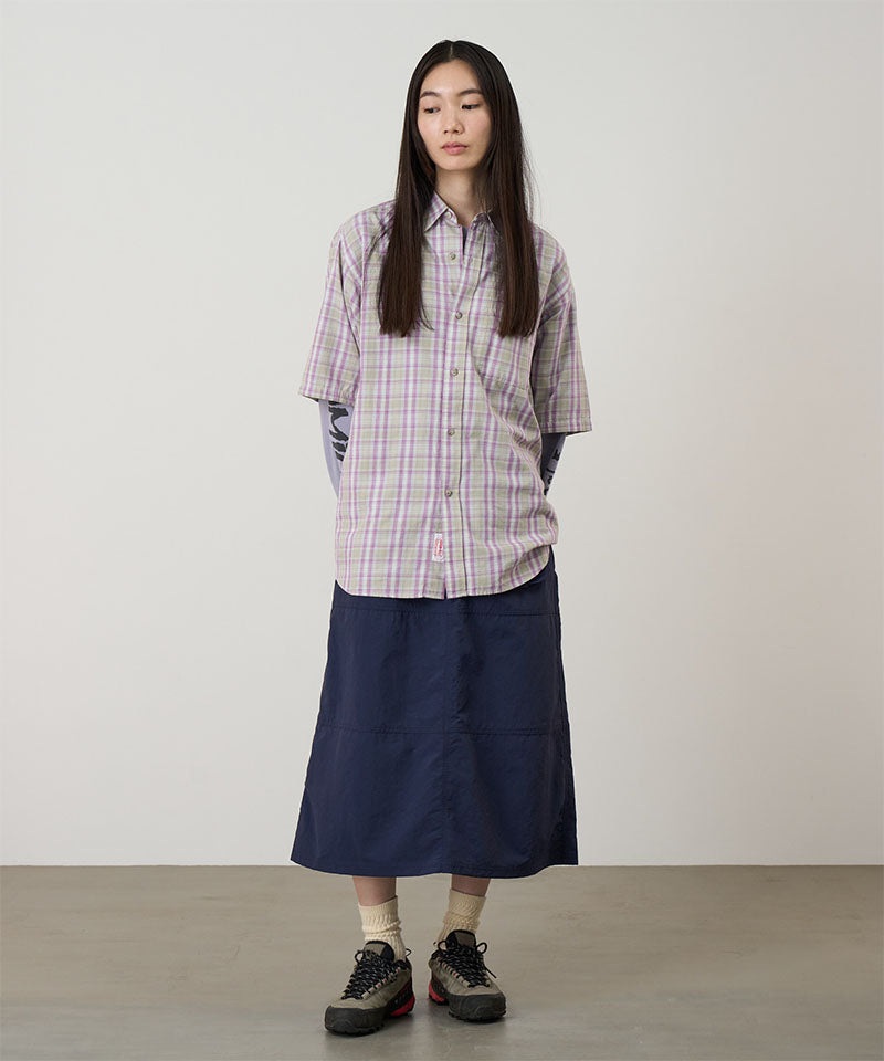 Model wearing a british navy Gramicci Nylon Utility Skirt and plaid shirt on a light-tone background.
