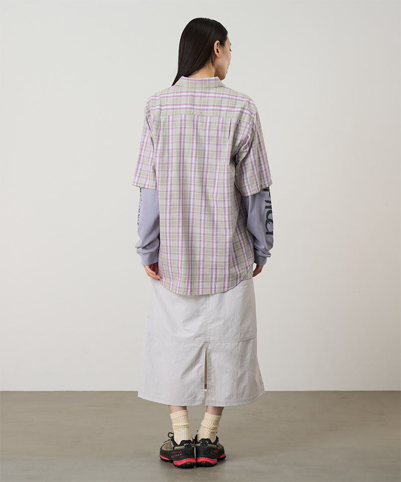 Back view of a model wearing a ecru colored Gramicci Nylon Utility Skirt and plaid shirt on a light-tone background.