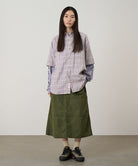 Model wearing a olive Gramicci Nylon Utility Skirt and plaid shirt on a light-tone background.