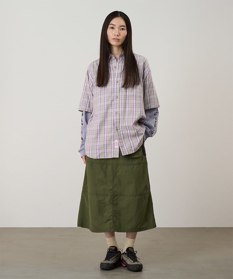 Model wearing a olive Gramicci Nylon Utility Skirt and plaid shirt on a light-tone background.