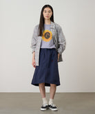 Model wearing a british anavy colored Gramicci Nylon Packable Midi Skirt and plaid shirt over a sunflower tee on a light-tone background.