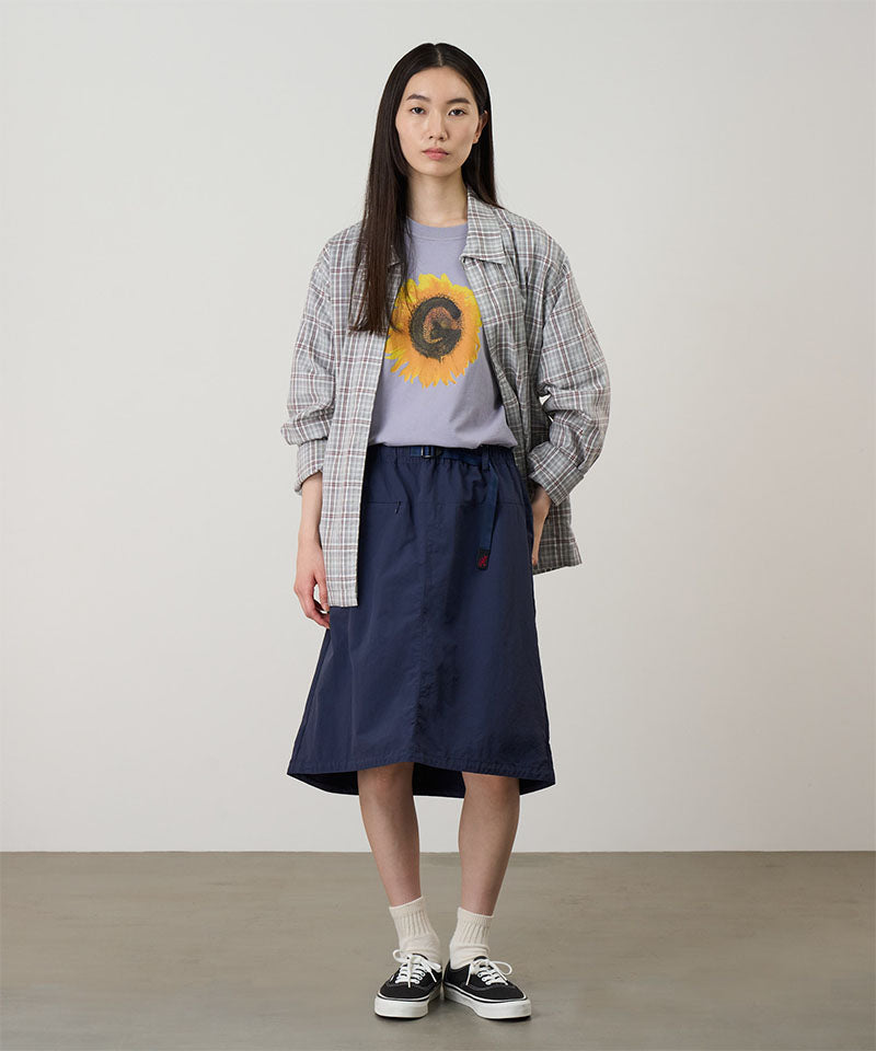 Model wearing a british anavy colored Gramicci Nylon Packable Midi Skirt and plaid shirt over a sunflower tee on a light-tone background.
