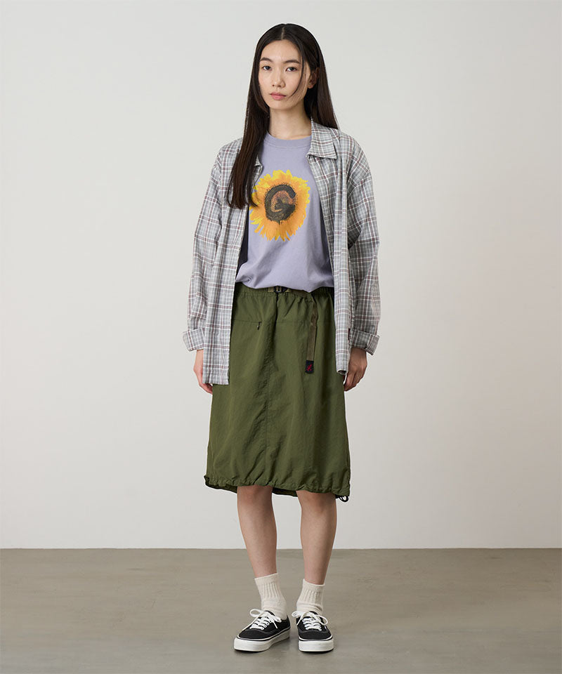 Model wearing an olive colored Gramicci Nylon Packable Midi Skirt and plaid shirt over a sunflower tee on a light-tone background.