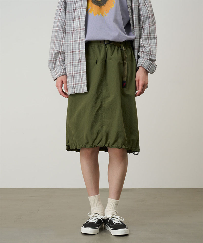 Model wearing an olive colored Gramicci Nylon Packable Midi Skirt and plaid shirt over a sunflower tee on a light-tone background.