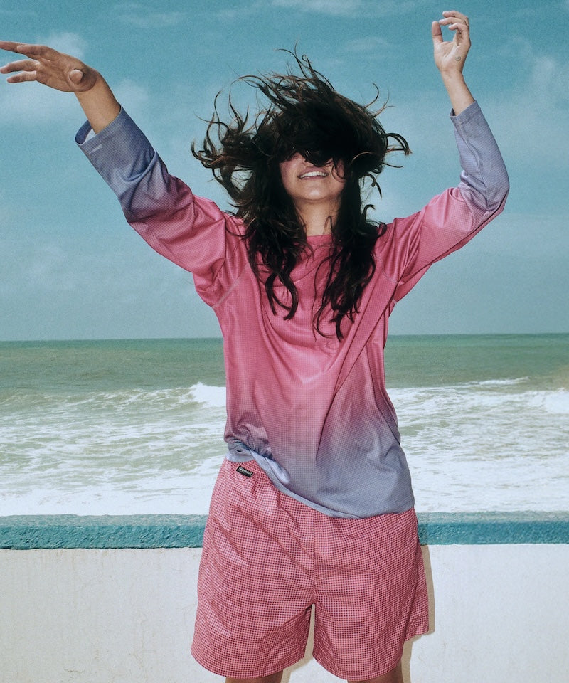 Person in pink shirt and shorts with arms outstretched on a beach