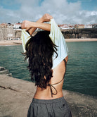 Person with a white shirt over their head by a waterfront with buildings in the background