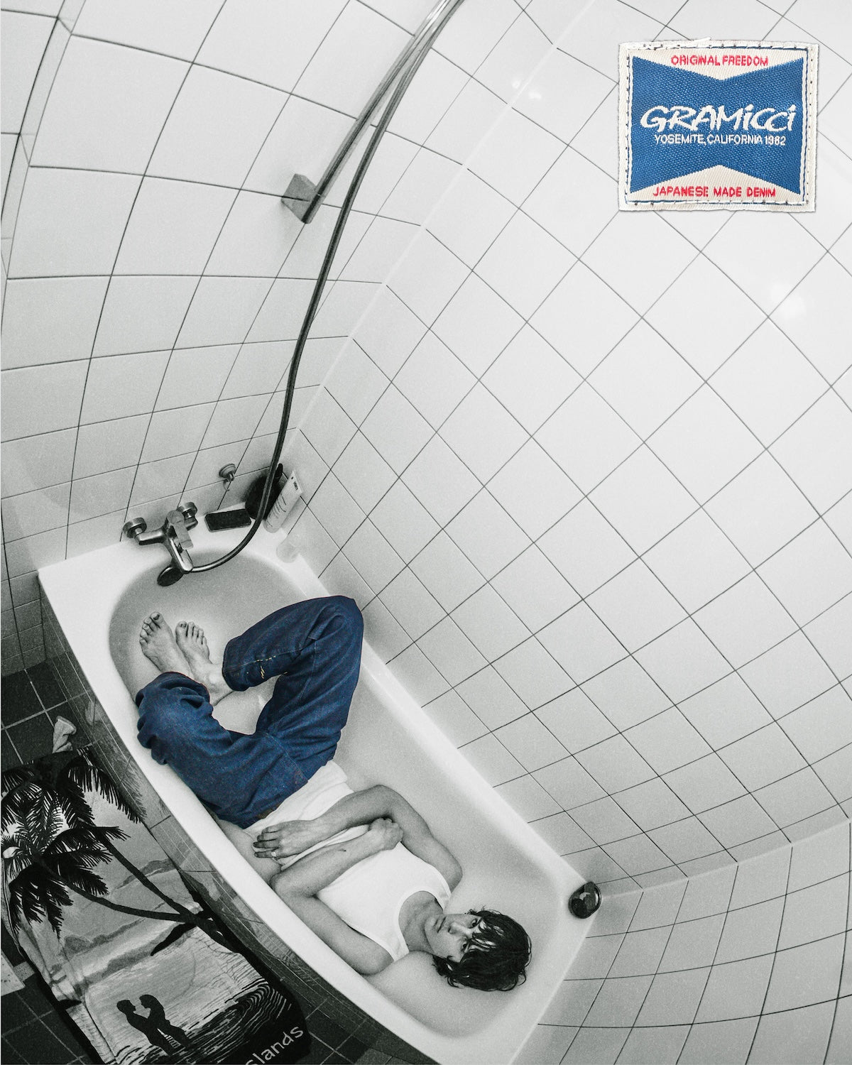 Gramicci relaxed-fit blue denim pants worn with a white tank top by a person lying in a dry bathtub, seen from a high angle.