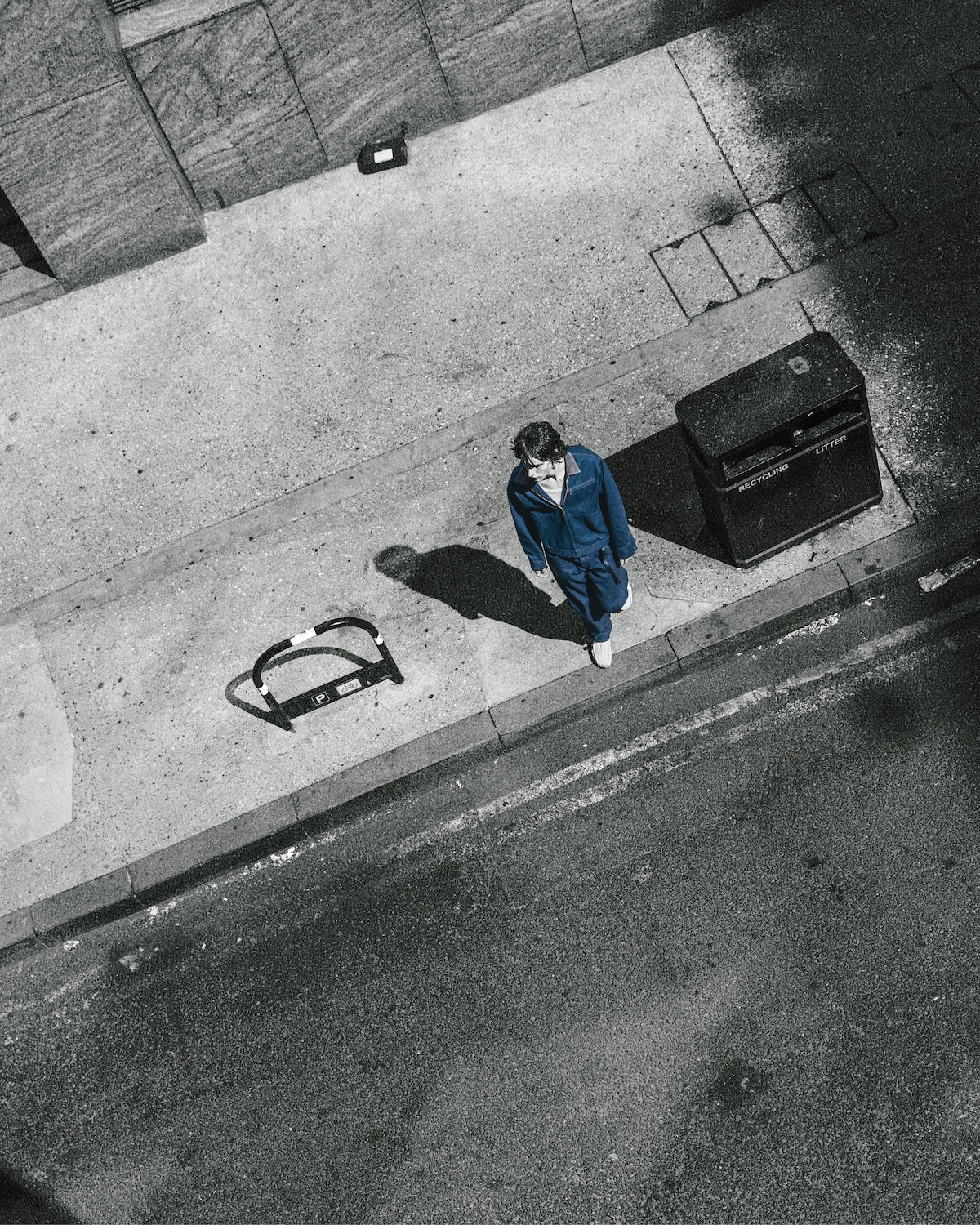 Gramicci relaxed-fit blue denim jacket and matching pants worn by a person walking on a city sidewalk next to a road, seen from a high aerial angle.