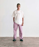 Gramicci white "Original Freedom" graphic T-shirt and relaxed-fit lilac colored pants worn by a person standing against a white studio background.   