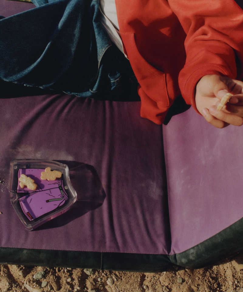 Person in red jacket holding a cookie over a purple blanket with a purple Gramicci shorts tray.