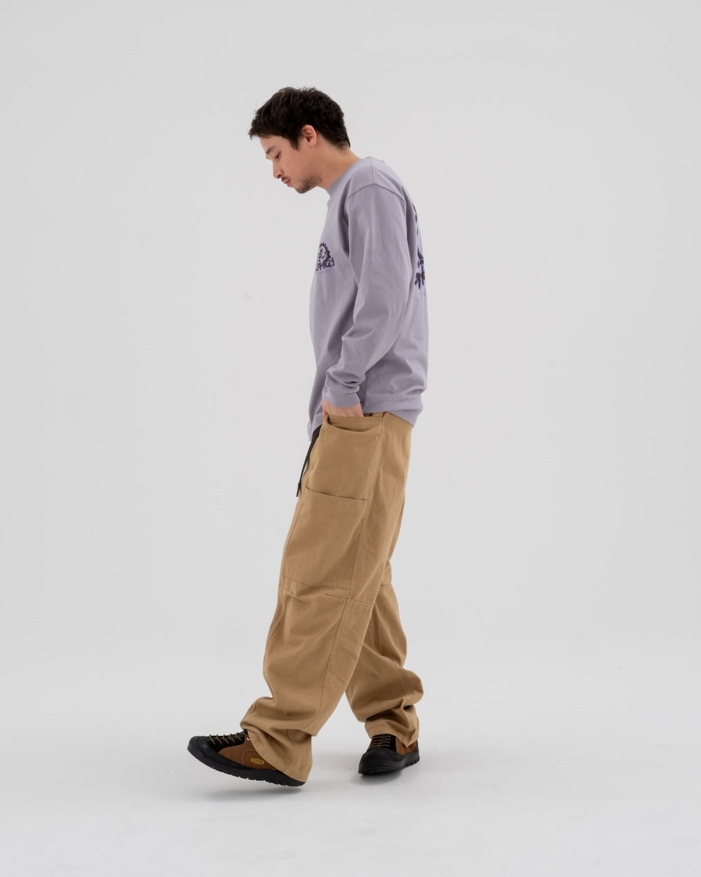 Model wearing tan Gramicci Pants and a lavender shirt on a light-tone background.