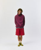 Person wearing a maroon pullover, red shorts, and Cactus colored Gramicci Dip Dye Socks against a light-tone background.